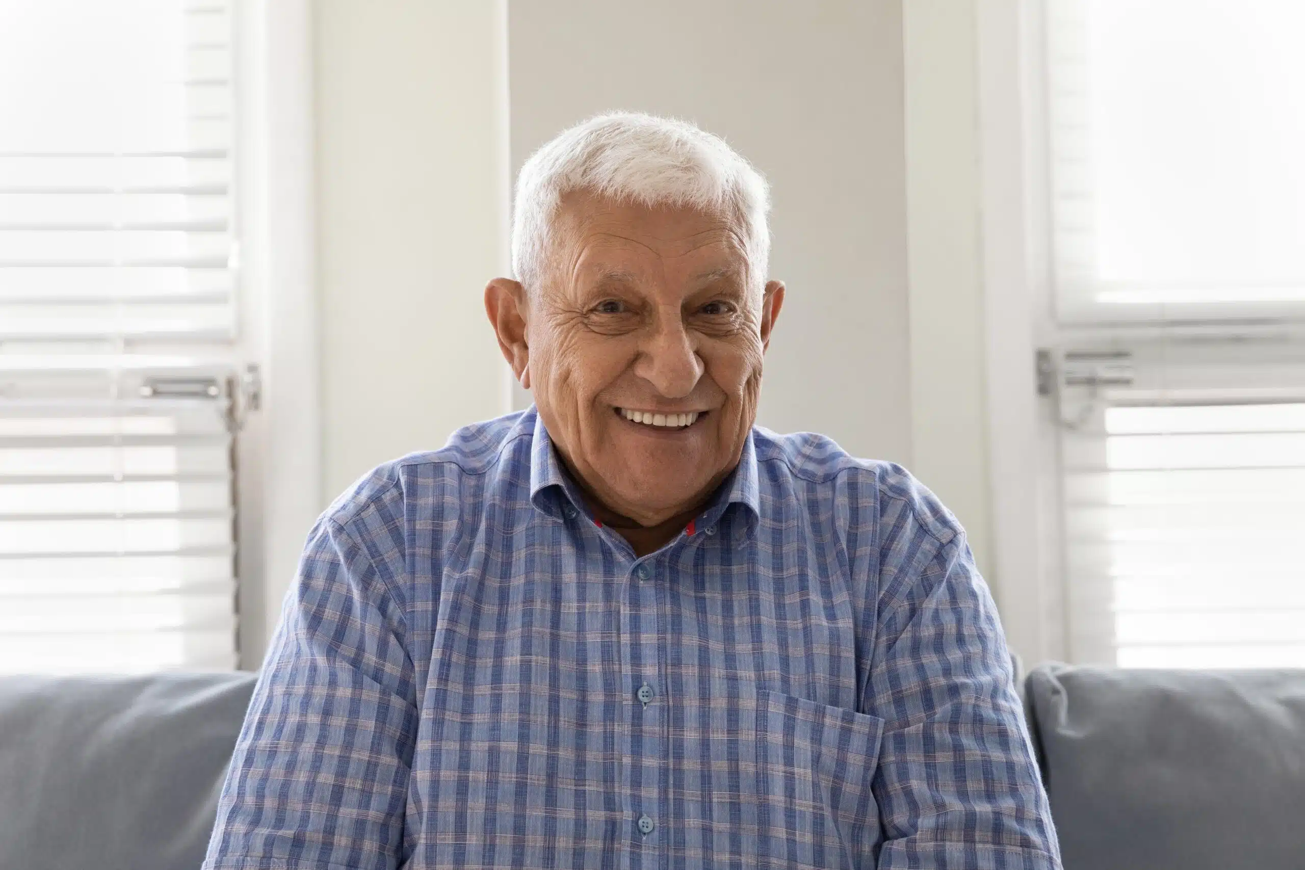 Older man with white hair smiling while sitting on a couch