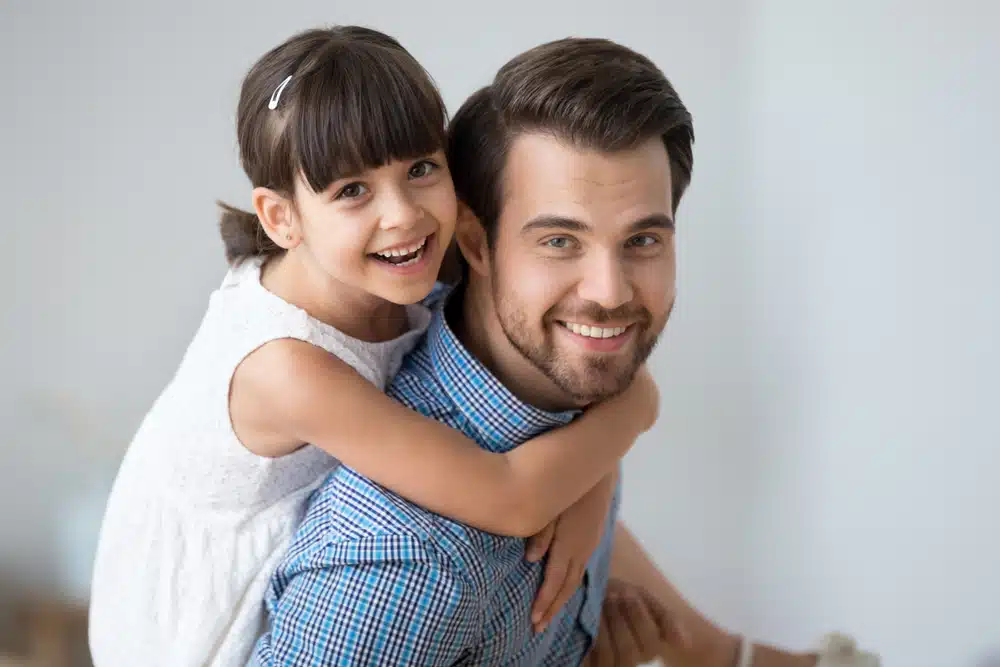 Smiling young girl hugging her father from behind