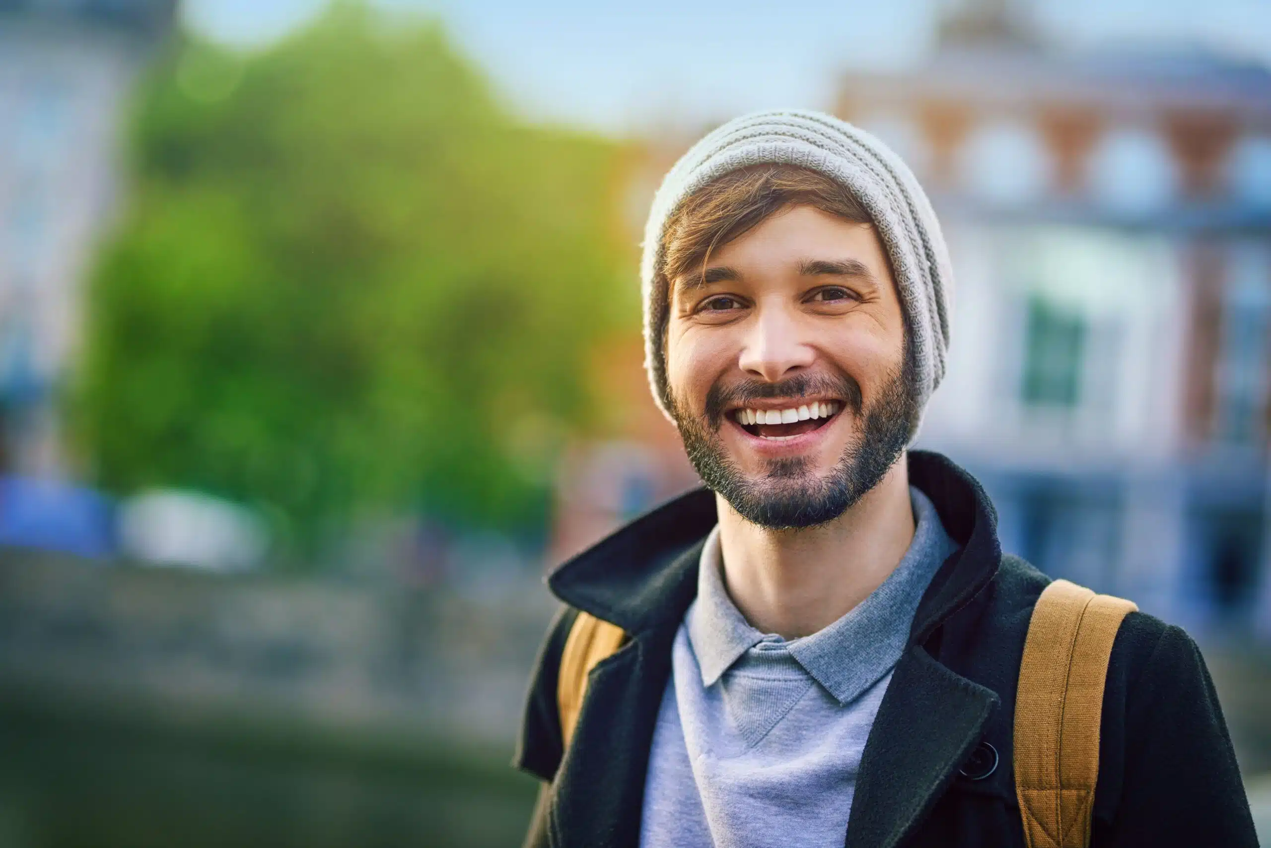 Man with a beard smiling outdoors while carrying a backpack
